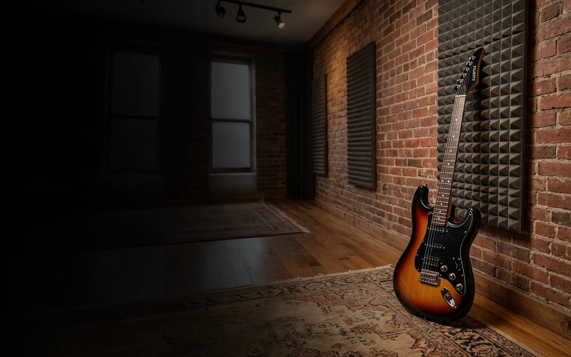 A sunburst Kadence electric guitar with a black pickguard, two single-coil pickups and a humbucker, leaning against a brick wall with acoustic foam panels in a dim practice room