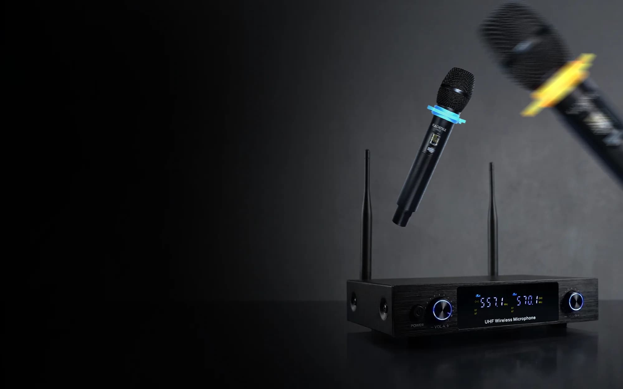 Kadence KB02 UHF wireless receiver with two antennas and both channel frequencies lit on its display, a handheld wireless microphone above it and a second one blurred in the corner