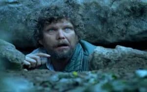 A man peering out from a narrow gap between rocks, looking uncertain