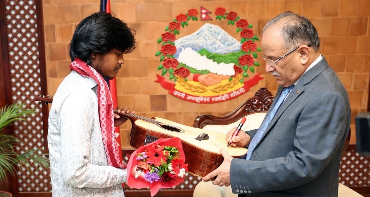 Nepal's Prime Minister signing the soundboard of an acoustic guitar held by a young musician, who is carrying a bouquet