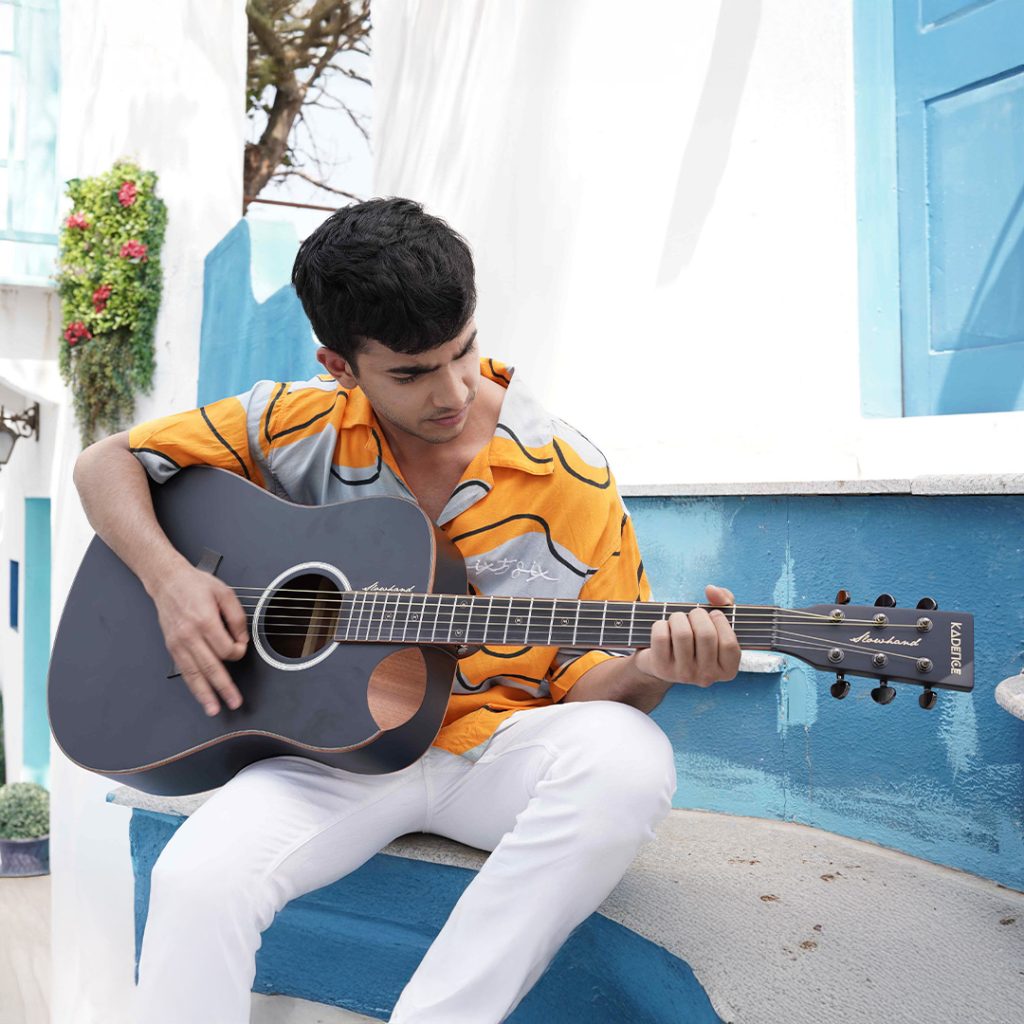 A young man playing a black Kadence acoustic guitar and showing, How Long Does It Take to Learn Guitar?